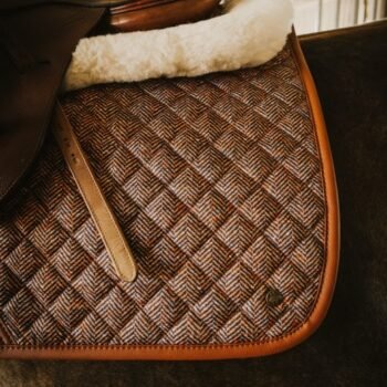Close-up do dorso de um cavalo com o protetor de sela Suadouro Tweed GP Heritage 16 Cypress, que apresenta um padrão de espinha de peixe acolchoado com acabamento em couro e lã. A textura detalhada e a costura são claramente visíveis.