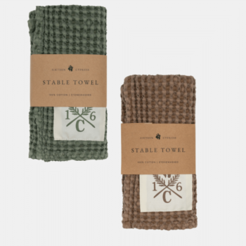 Duas toalhas dobradas de algodão com textura de waffle, uma verde e outra marrom, cada uma com uma etiqueta bege 