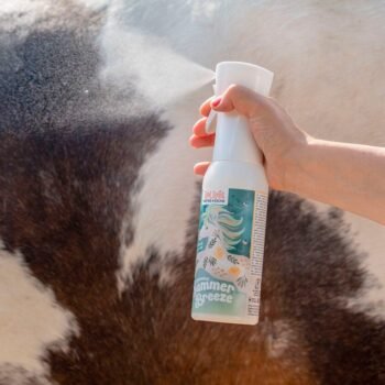 Uma mão pulveriza o Repelente Lilla Livet Botanical Summer Breeze, com uma ilustração de um cavalo, na pelagem em preto e branco de uma vaca ou cavalo ao ar livre.